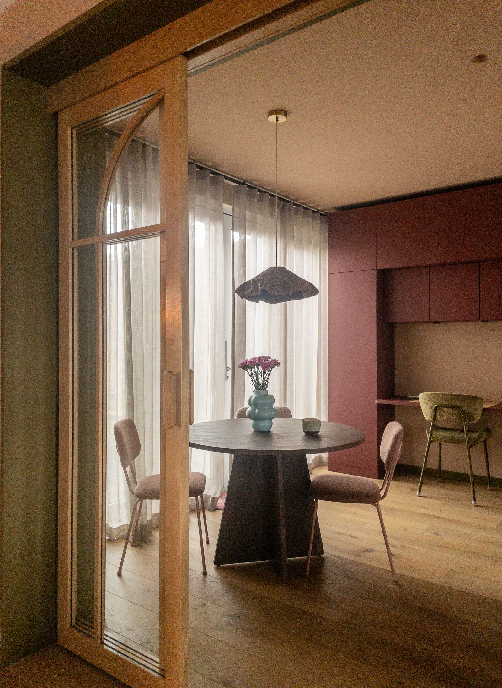 Doorkijk naar een warme eetkamer met bordeauxrode kastenwand, ingericht door Lion House Interior